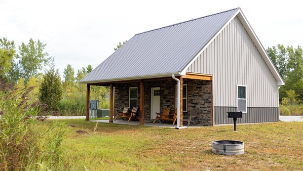 A single-story building with a sloped roof, a covered porch with chairs, and a stone exterior.