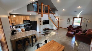A spacious living area with a kitchen, a dining table, and a staircase leading to an upper level.