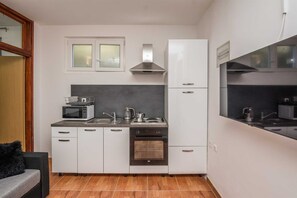 Compact kitchen with modern design, white cabinetry, and a sleek countertop, featuring a microwave, oven, sink, and stovetop.