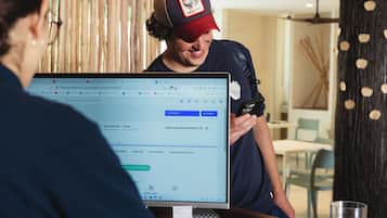 A person using a laptop at a wooden table in a room with a woven light fixture and vertical wooden panels.