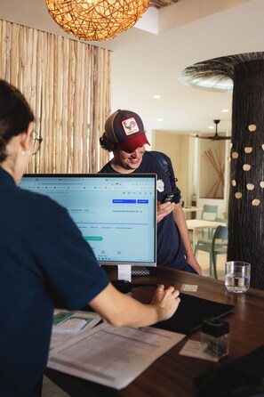 Eine Person benutzt einen Laptop an einem Holztisch in einem Raum mit einer gewobenen Leuchte und vertikalen Holzpaneelen.