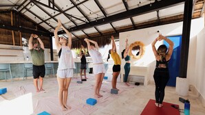 A group of people performing a yoga or stretching exercise in a covered outdoor area with mats and blocks. - SUUT Hostal Boutique (Playa del Carmen)