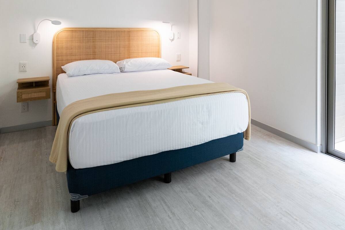 Een moderne hotelkamer met een bed, een plafondventilator, een nachtkastje en een groot raam.