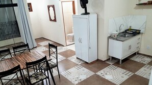 Zona de menjador amb taula i cadires de fusta, un armari blanc i un paviment de rajoles.