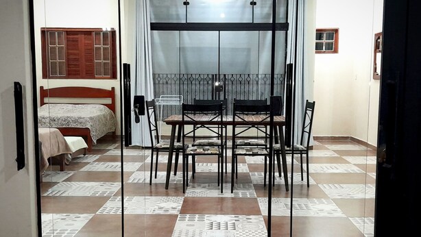 Una habitació amb un llit, taula de menjador amb cadires i una finestra amb persianes de fusta.