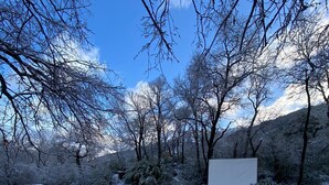 Een besneeuwde buitenruimte met een houten terras en een omheind tennisveld.
