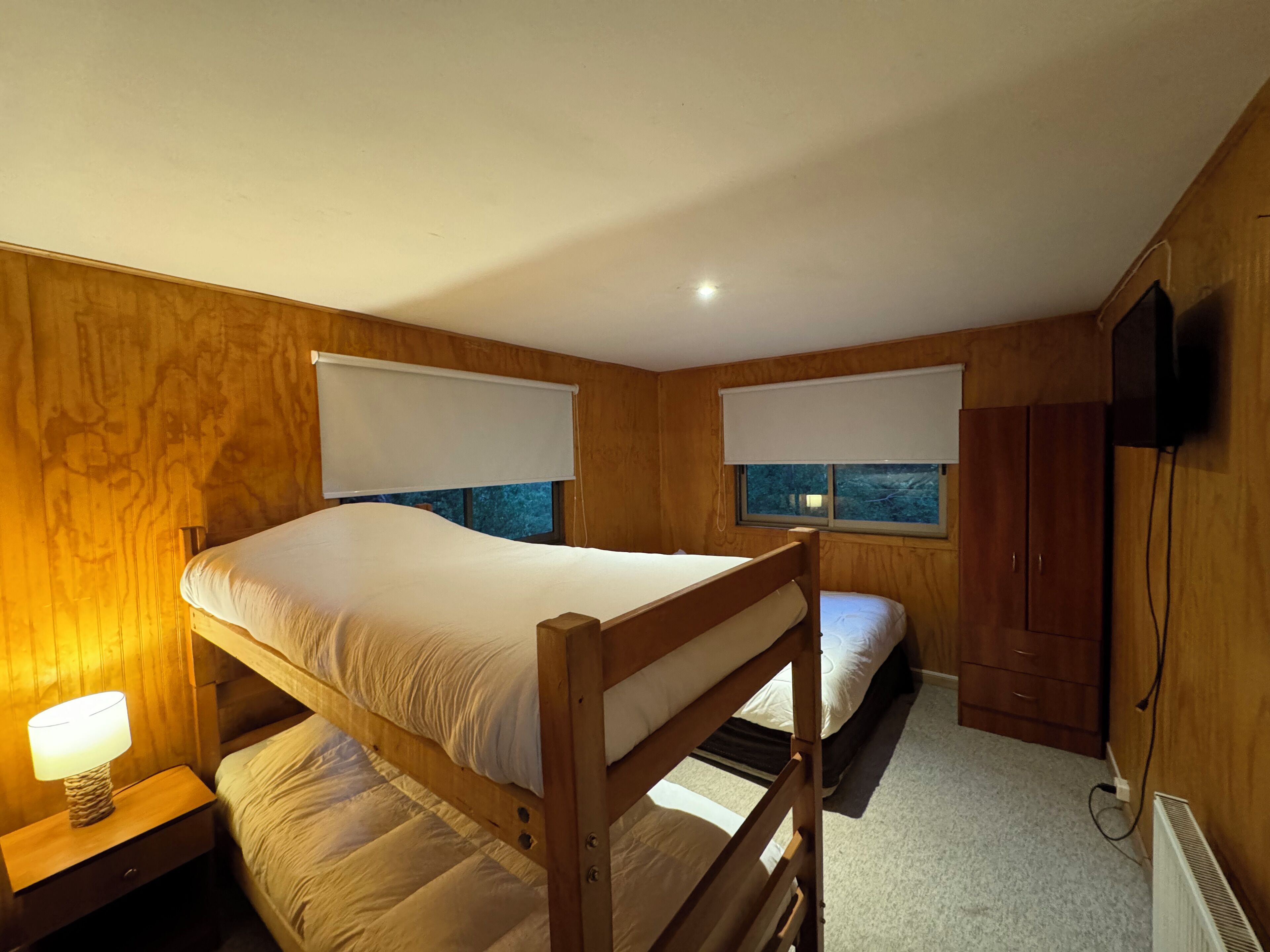 Ein Zimmer mit zwei Etagenbetten, Holzwänden, einem kleinen Nachttisch mit Lampe, einem Kleiderschrank und einem an der Wand montierten Fernseher.