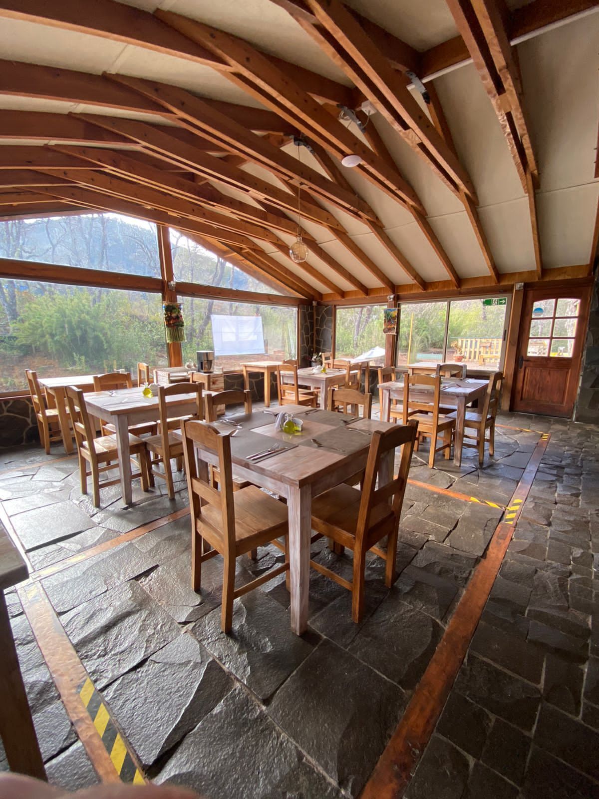 Ein rustikaler Essbereich aus Holz mit Steinböden und großen Fenstern mit Blick auf einen bewaldeten Bereich.