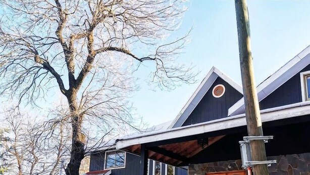 Een huis met twee verdiepingen, een stenen gevel, een houten terras en een met sneeuw bedekte grond.