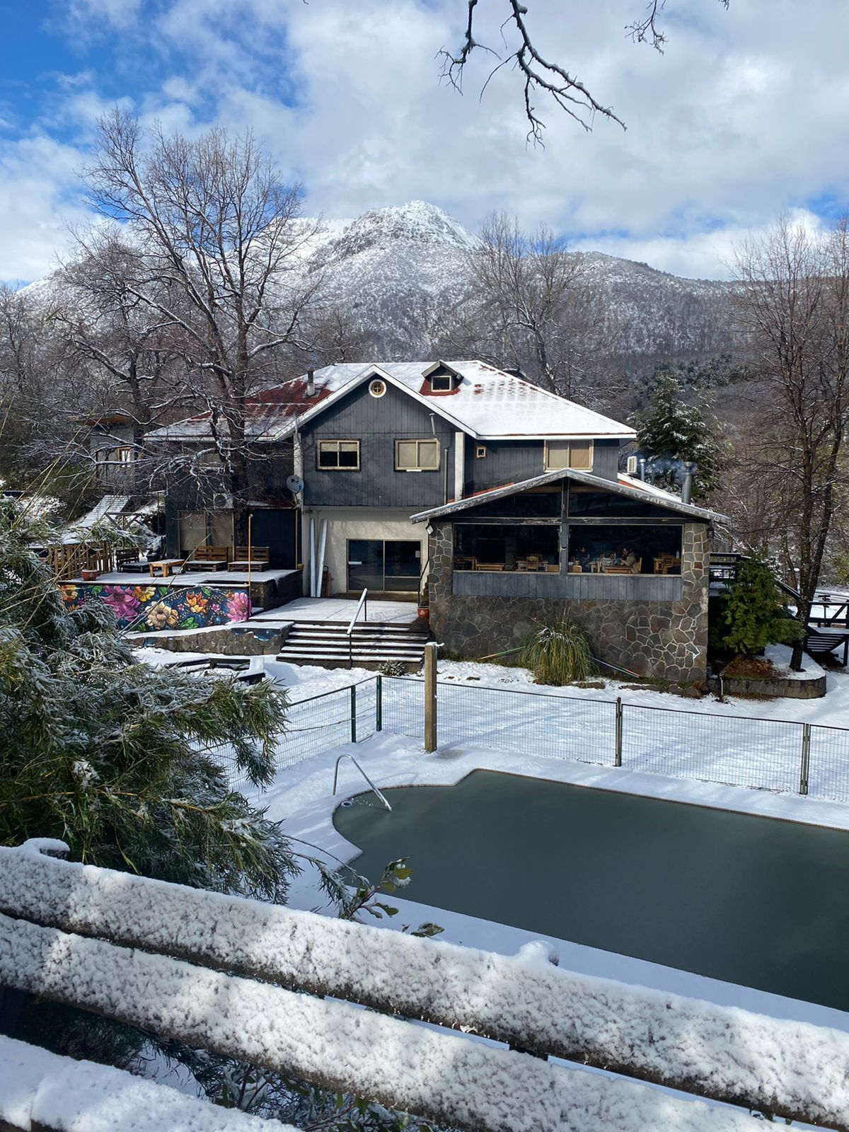 Una casa grande con fachada de piedra, una piscina y vistas a montañas nevadas.