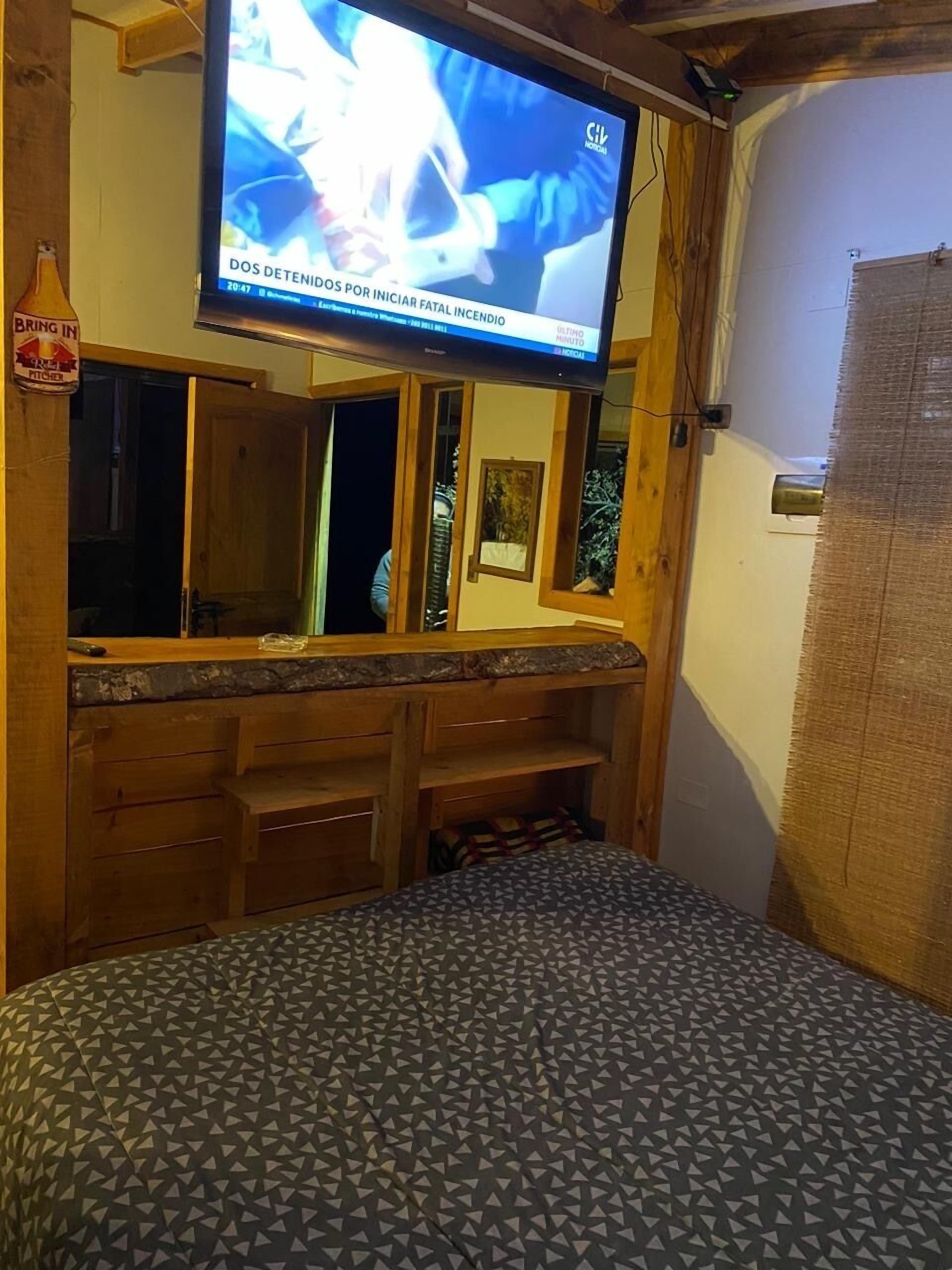 A room with a bed, wooden headboard, a television mounted above the bed, and a wooden cabinet below.