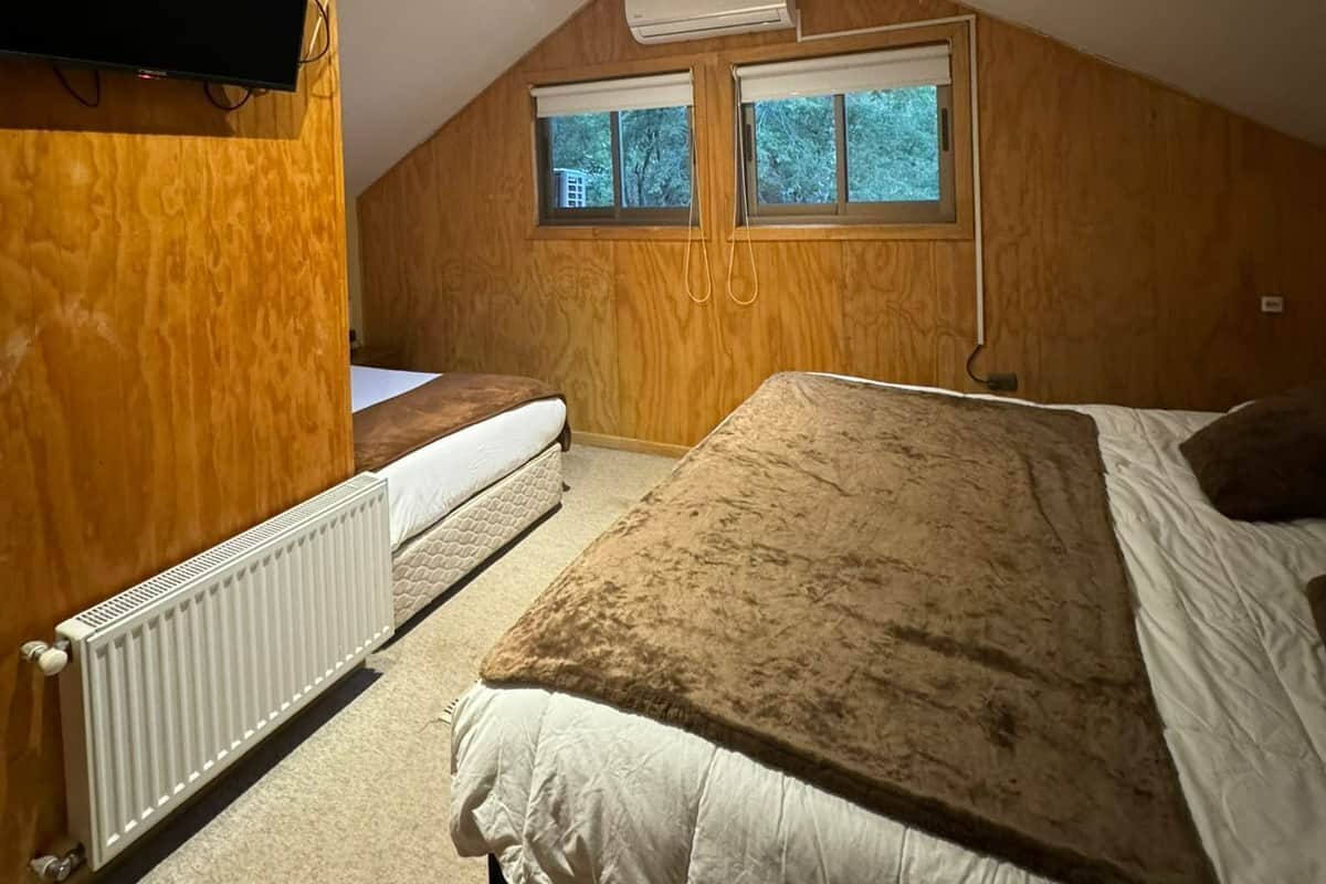 Ein Schlafzimmer mit schrägverdeckter Decke, Holzwänden, einem Bett, einem Heizkörper und einem an der Wand montierten Fernseher.