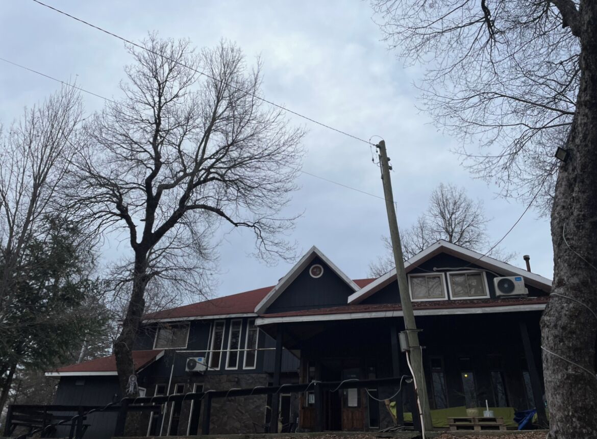 A two-story building with a dark facade, a red roof, and a porch area.