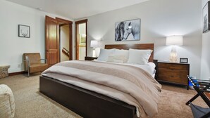 A bedroom with a large bed, wooden headboard, two bedside tables with lamps, a chair, and a ceiling fan.