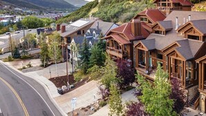 A cluster of wooden cabins with pitched roofs, surrounded by trees and a view of a town and mountains in the background.