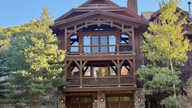 A multi-story wooden house with a stone foundation, large windows, and a garage.