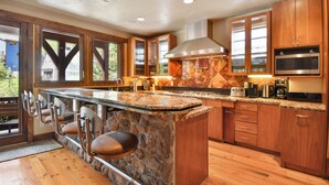 A modern kitchen with a large island, wooden cabinets, and a stone backsplash.