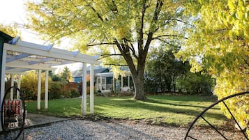 Een overdekt terras met een pergola, een grote boom en een grindpad.
