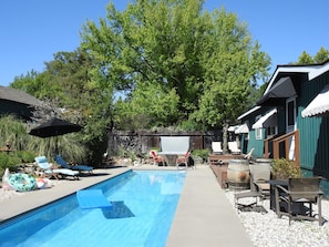 Une piscine entourée d’arbres et d’une clôture en bois, avec des chaises longues et des parasols à proximité.
