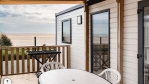 A covered outdoor area with a table and chairs, a wooden deck, and a view of the beach. - ZEcamping 4* animé 2km plage parc aquatique locatif TV clim 36m2 (La Faute-sur-Mer)
