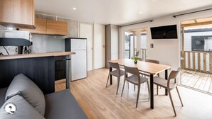A compact kitchen with wooden cabinets, a built-in fridge, and a dining area with a table and chairs. - ZEcamping 4* animé 2km plage parc aquatique locatif TV clim 36m2 (La Faute-sur-Mer)