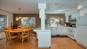 Una cocina moderna con armarios blancos, una mesa de comedor de madera e iluminación colgante.