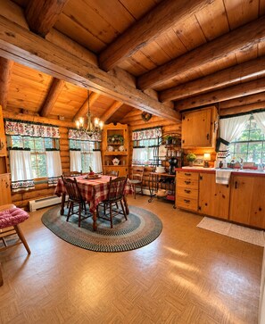 A wooden cabin interior with a dining area, kitchen, and a fireplace.