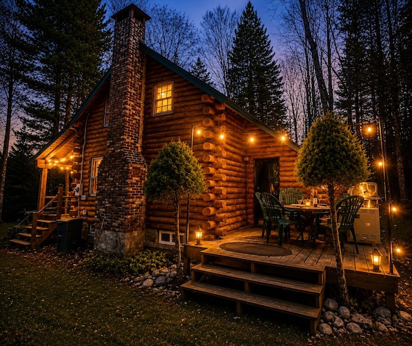 A log cabin with a stone chimney, a porch with outdoor seating, and a staircase leading to the entrance.