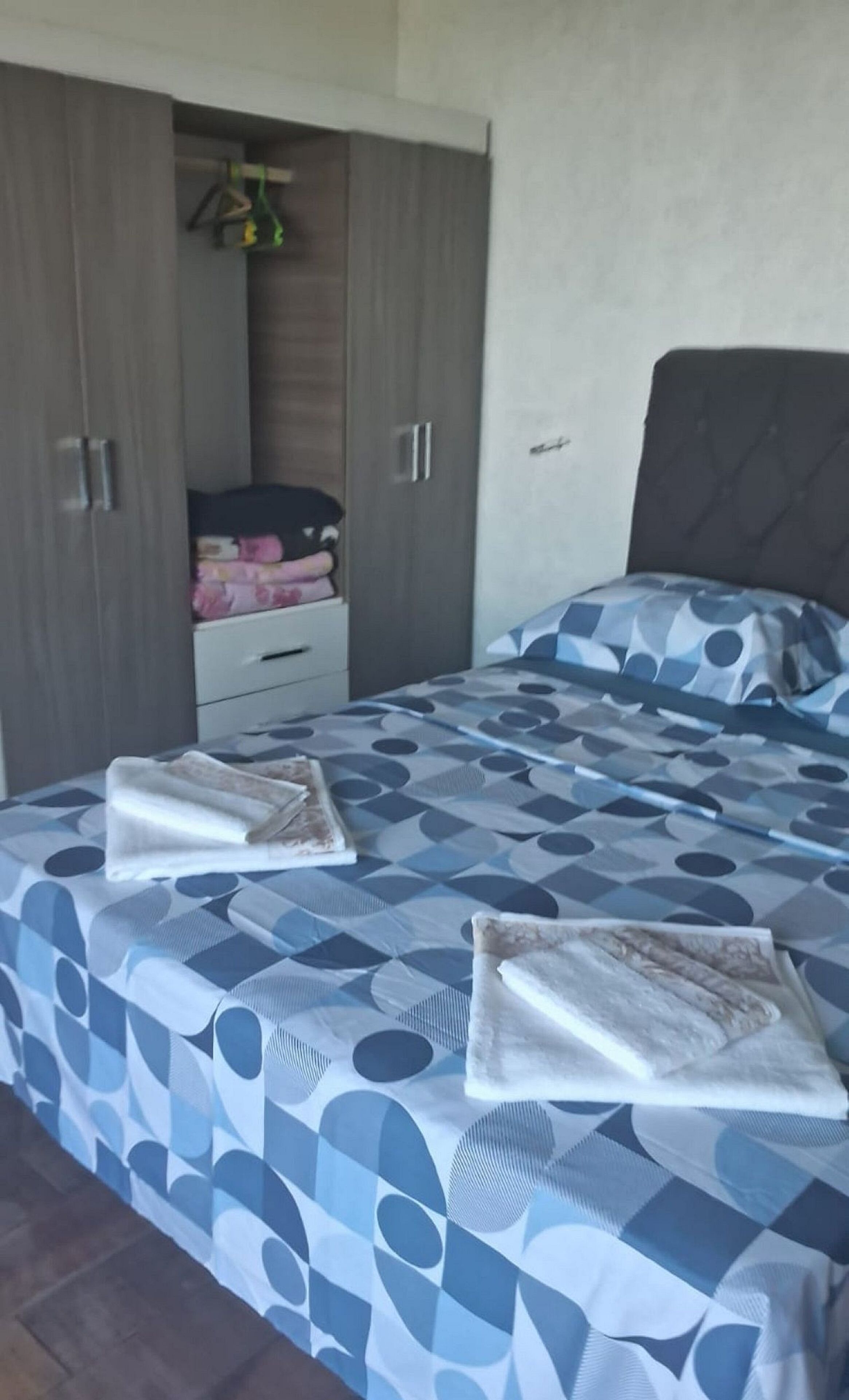 A bedroom with a bed, two nightstands, a wardrobe, and a hanging rack.