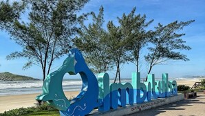 Une grande sculpture bleue portant les inscriptions « Imbituba » et « CAPITAL NACIONAL DA BALEIA FRANCA », située sur une promenade pavée au bord de la plage.