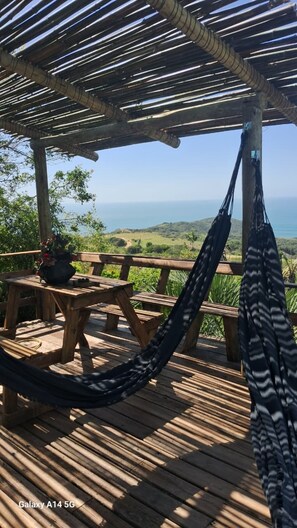 A wooden deck with a hammock, picnic table, and potted plant. - Refúgio Farol Ponta do Catalão - SC (Imbituba)