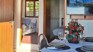 Un coin repas avec une table dressée pour deux personnes, un arrangement floral en guise de centre de table et un téléviseur fixé au mur.