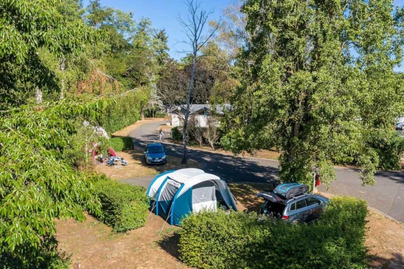 Een kampeerterrein met een tent, een auto en een pad.
