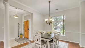 A dining room with a wooden table, white chairs, a chandelier, and a window with a view. - 3 Mi to Oglethorpe Mall: Home w/ Fenced Yard! (Savannah)
