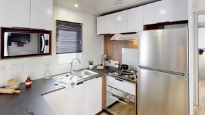 Eine moderne Küche mit weißen Schränken, Edelstahlgeräten, einem eingebauten Backofen und einem Fenster mit Jalousien.