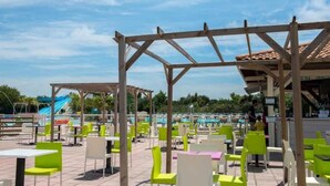 An outdoor pool area with multiple seating arrangements, including tables and chairs, under a wooden pergola structure.