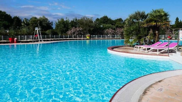 A clear blue swimming pool with lounge chairs and a ladder.