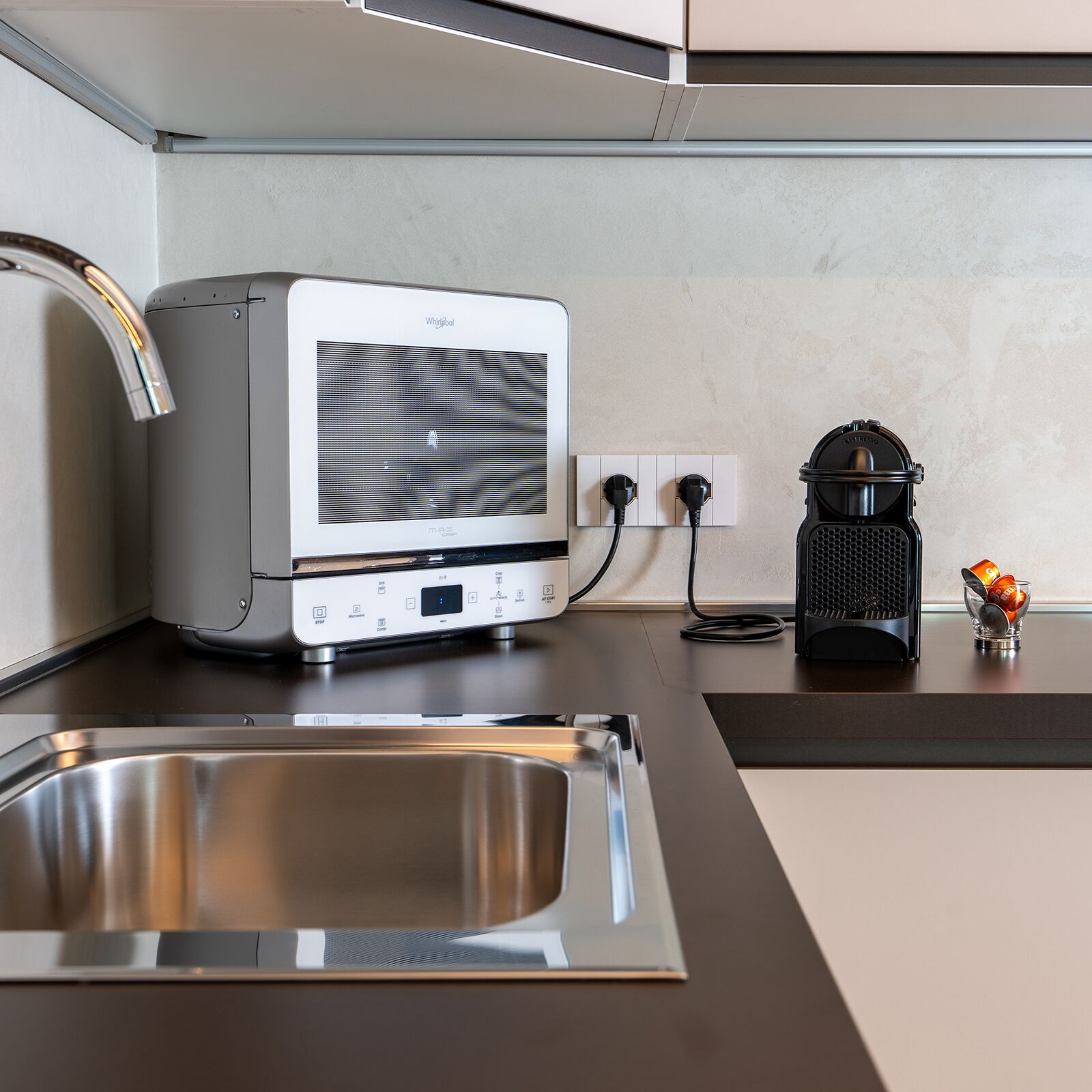 A kitchen with a built-in microwave, a coffee maker, and a stainless steel sink.