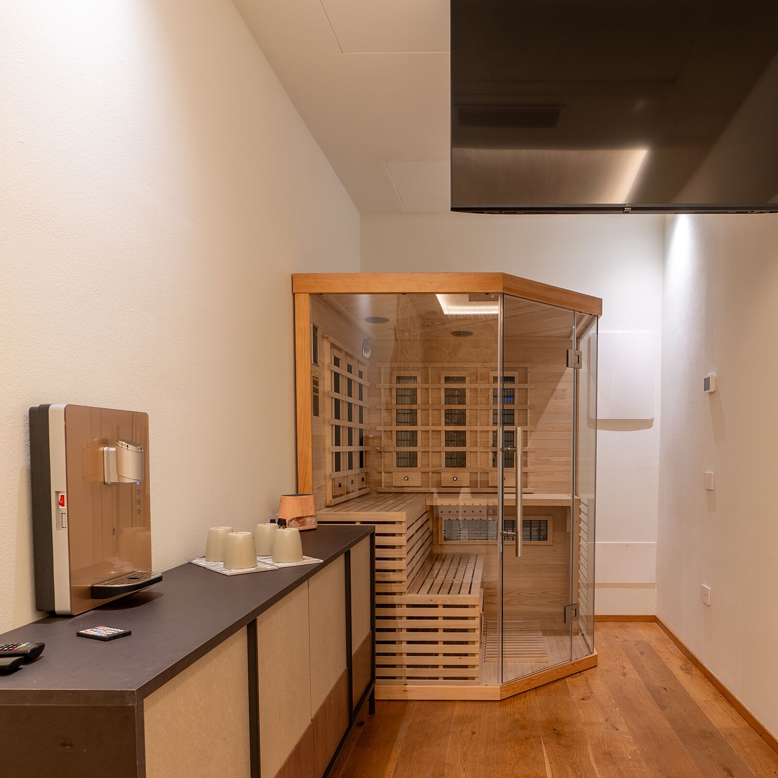 Une salle de bain moderne avec un comptoir d’accueil en bois, un sauna vitré et un grand miroir.