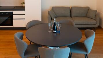 A modern dining area with a round table, grey upholstered chairs, and a sofa in the background.