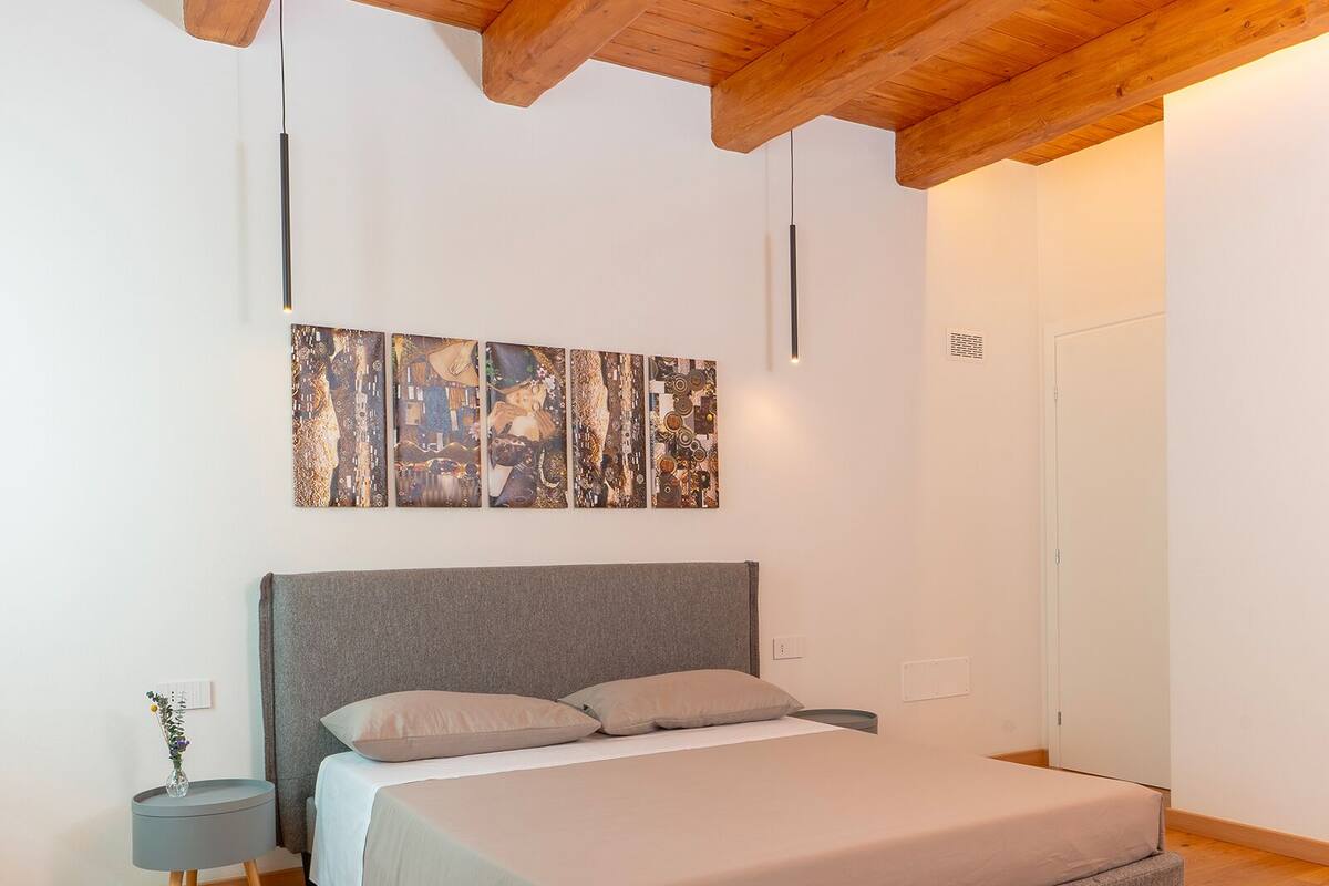 A bedroom with a bed, a nightstand, a wall art piece, and a wooden ceiling.