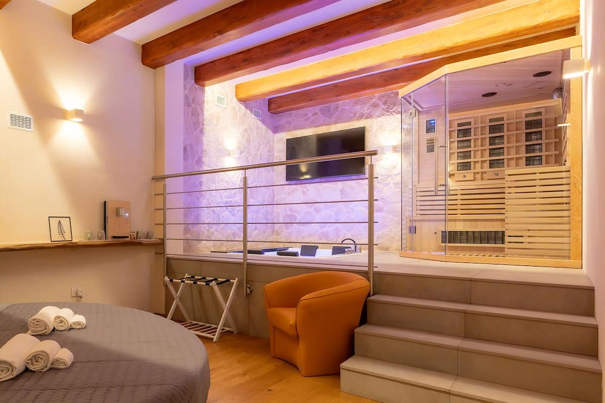 A bedroom with a bed, a chair, a wooden floor, a window, and a staircase.