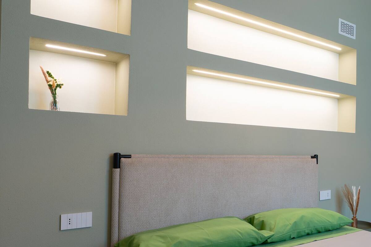 A neatly arranged hotel room with a bed, green pillows, a bedside table, and wall-mounted light fixtures.