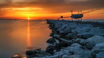 Ein Sonnenuntergang über einem ruhigen Meer mit einer felsigen Küste und einer Brücke mit Kränen.
