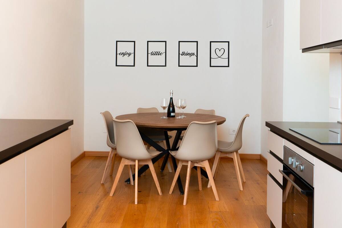 A modern kitchen with a wooden ceiling, a dining table with four chairs, and a kitchen island with a stove.