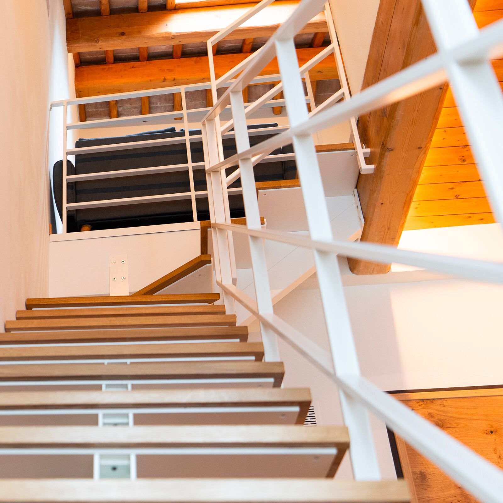Una escalera de madera con barandillas blancas y vistas a una habitación con cama y ventana.