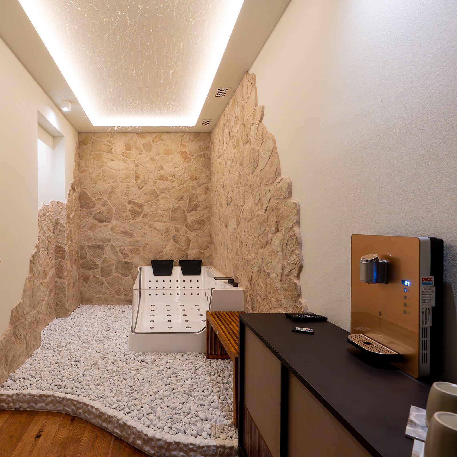 A modern spa room with a stone wall, a massage table, a wooden bench, and a sauna.