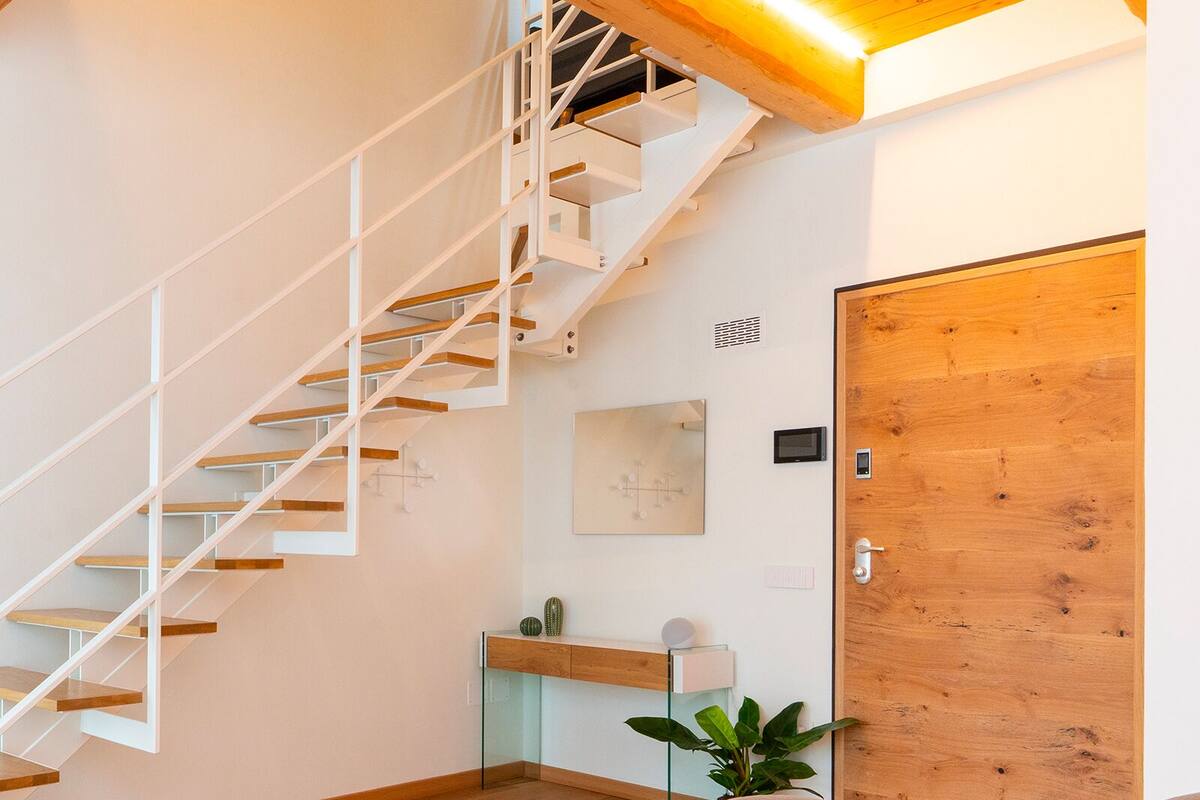 A modern interior with a wooden staircase, a dining area, and a wooden door.