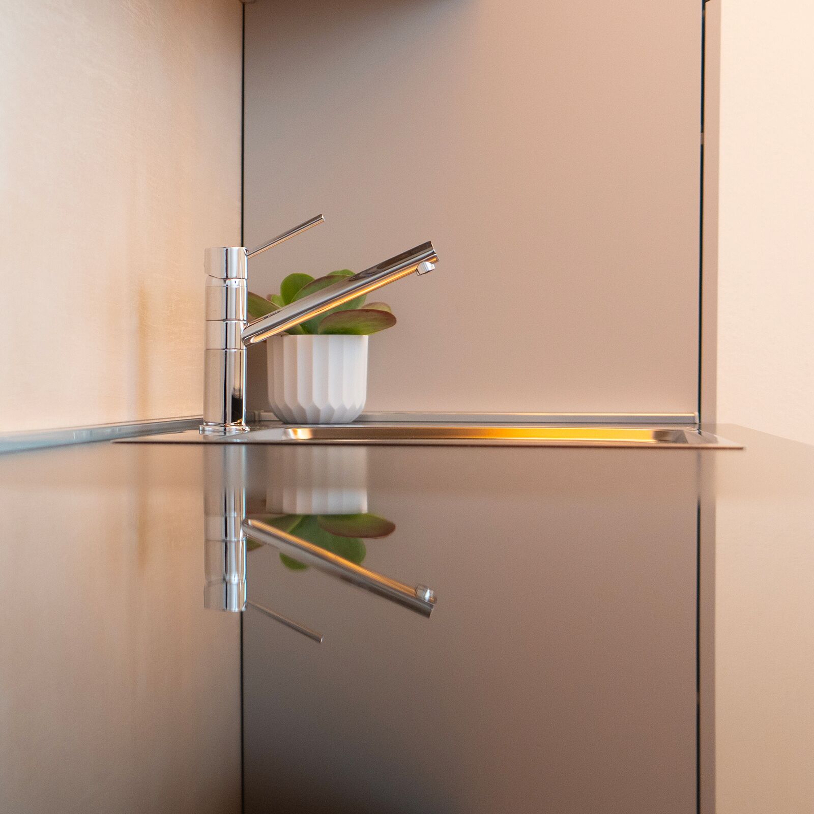 A modern bathroom with a chrome faucet, a white textured basin, and a potted plant.