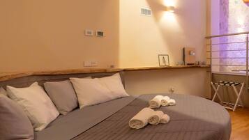 A bedroom with a large bed, a wooden ceiling, a stone wall, and a small shelf with a picture frame and a bottle.